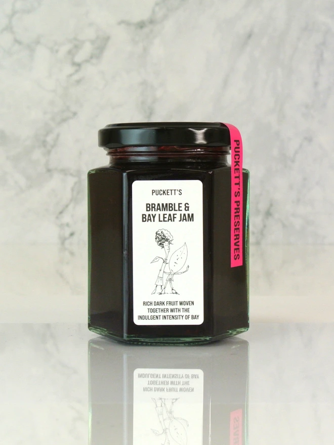 bramble and bay leaf jam. a jar of bramble and bay leaf jam photographed on a marble background.