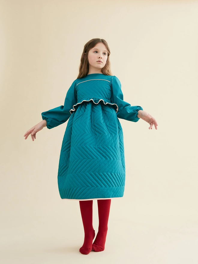 Made from a cotton sateen in our rich ‘Peacock’ colourway. Featuring quilting to the bodice and skirt with contrast edging to bodice, peplum edge and hem. Elastic to cuff.