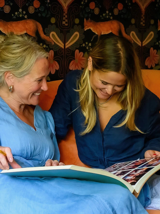 A mother & daughter smile as they look at the photos in a wedding photo album together.
