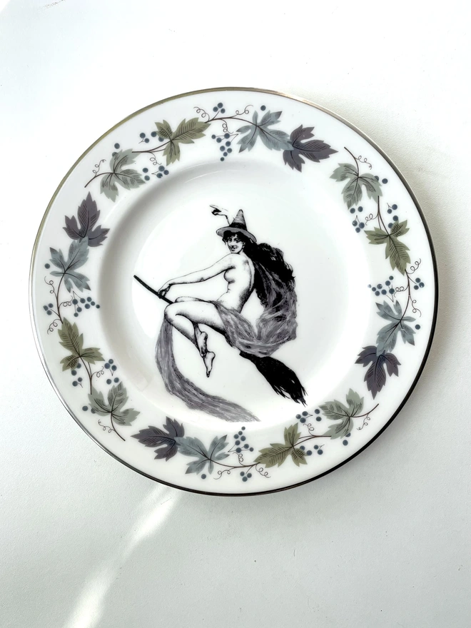 vintage plate with an ornate border, with a printed vintage illustration of a witch on a broomstick in the middle 