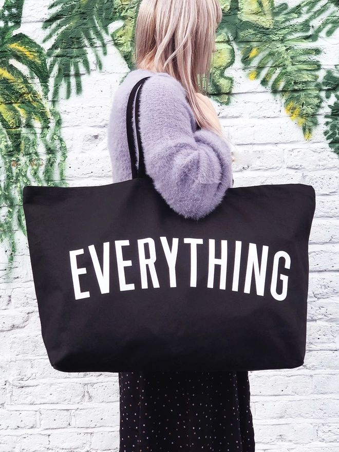 model carrying an oversized black canvas tote bag with everything slogan