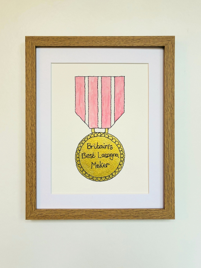 A hand painted Gold medal artwork with pink ribbon and a personalised embroidered message reading Britain's best Lasagna Maker