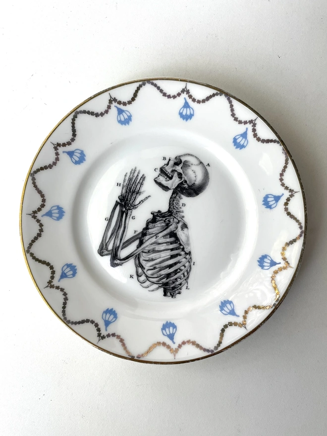 a vintage ornate plate that has a patterned border, and in the centre i have print a black and white illustration of praying hands skeleton in a vintage style