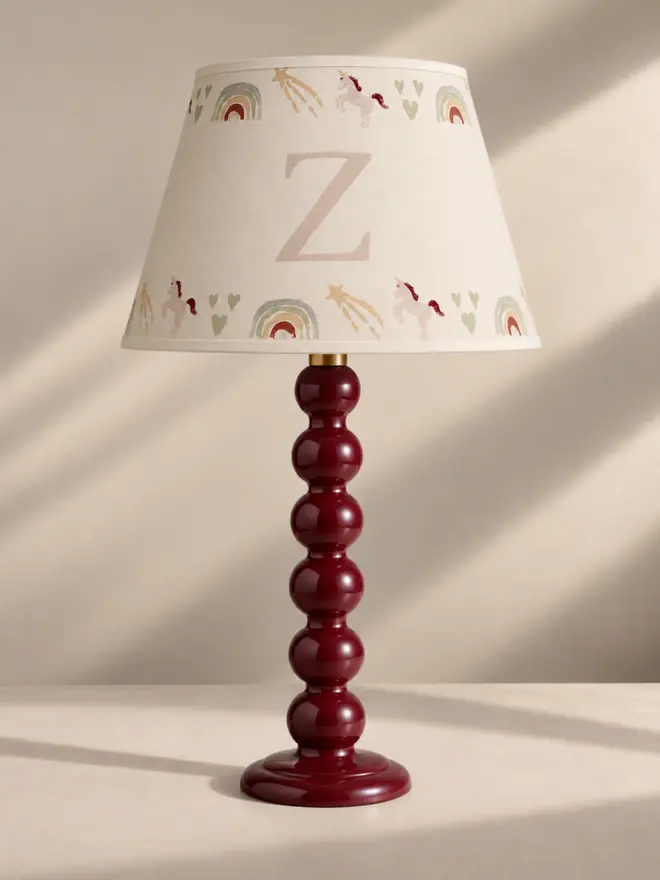 Personalised unicorn lampshade with initial Z, decorated with hand-painted unicorns, rainbows, hearts and shooting stars, styled on a red bobbin table lamp.
