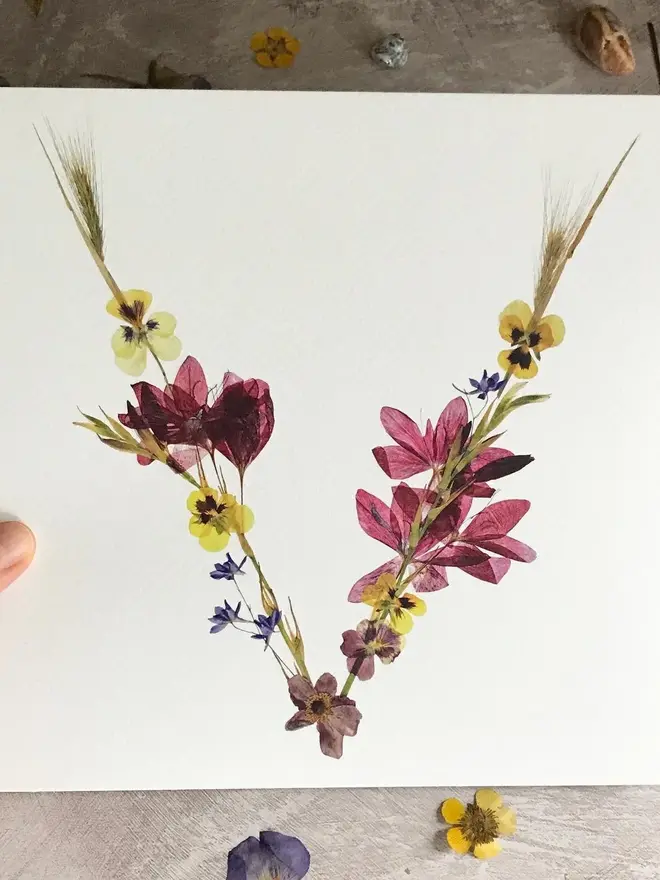 Pressed Wildflower Letter Print, a wildflower alphabet letter print held against a flowery backdrop. 