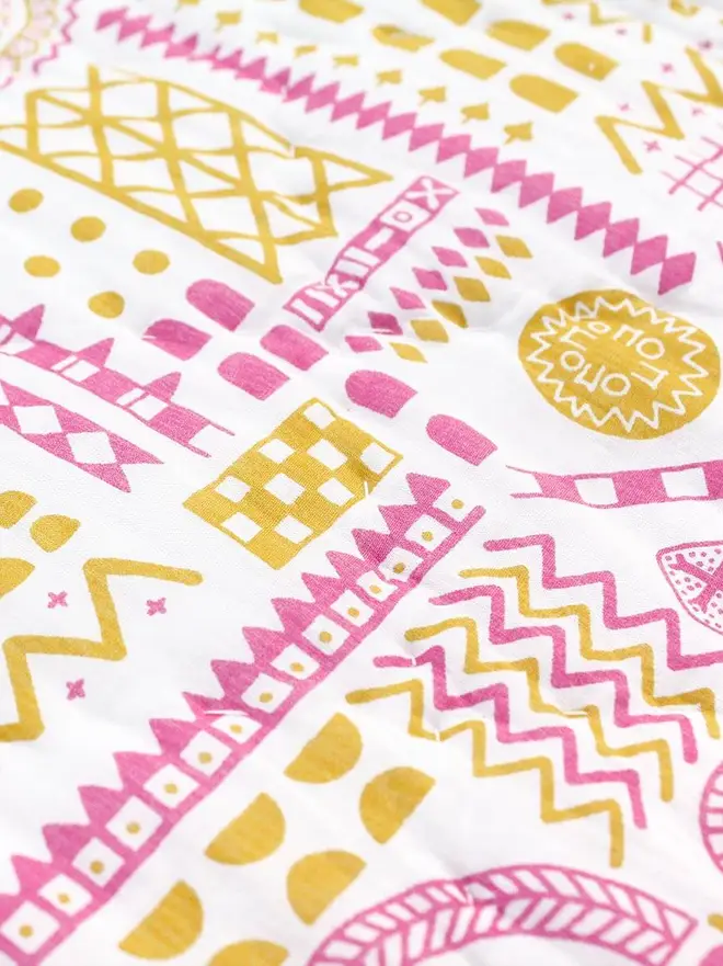 Fairy Chimney Quilt, a pink and yellow quilt sitting on a bed in a bedroom. 