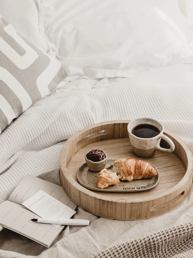 wooden breakfast tray holding a croissant, coffee and open journal