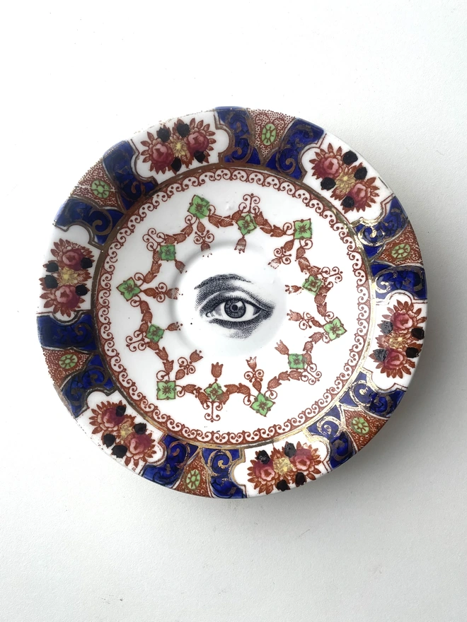 a very ornate vintage plate with high pattern and in the centre is a vintage black and white illustration of an eye