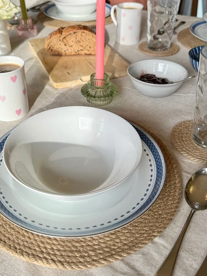 Close up of a round woven seagrass neutral placemats, with a flowery bowl on top shown on a light surface. 