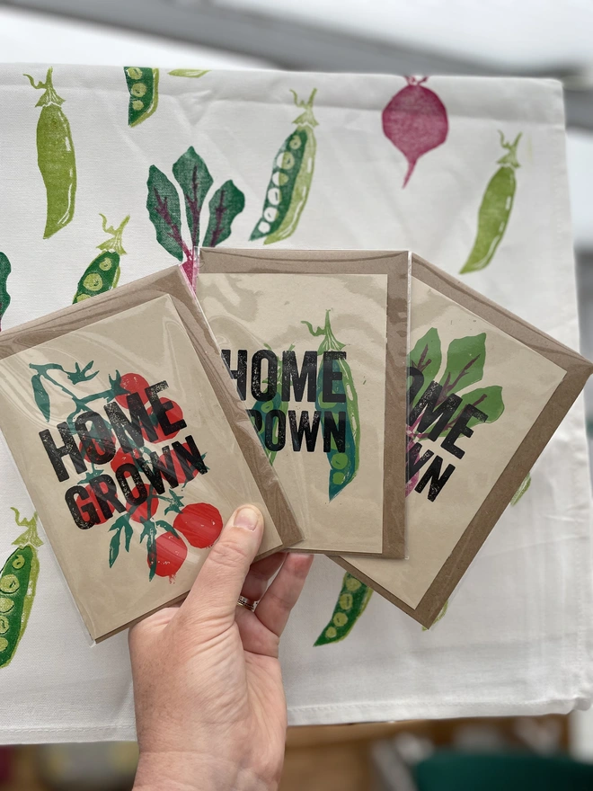 'Home Grown' Pea Lino Garden Print. A display of handmade pea themed cards arranged on a wooden table. 