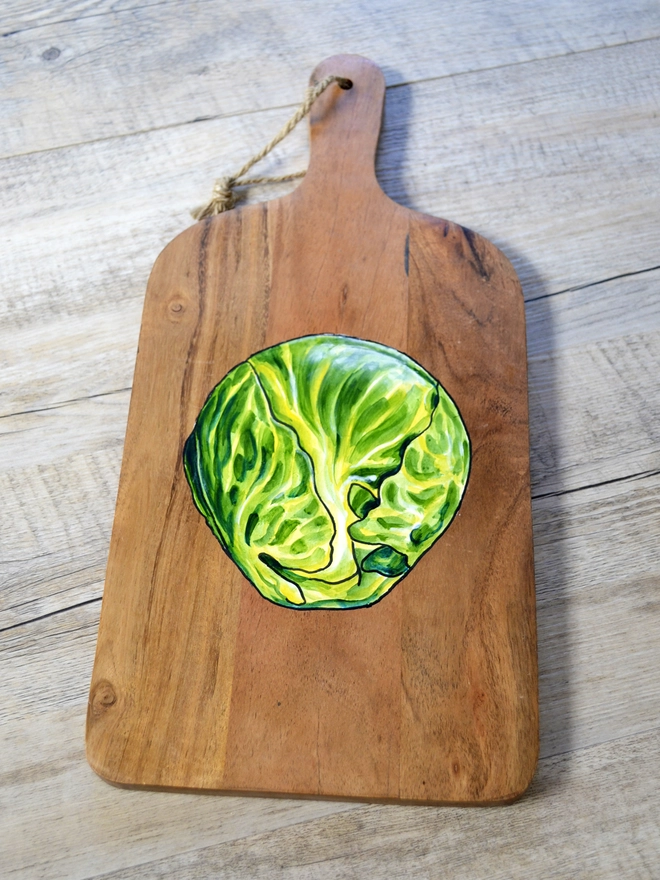 A wooden serving board with a handpainted design of Brussels sprouts