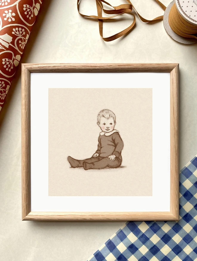 a photograph of a hand drawn vintage style baby personalised portrait framed in a square oak frame laid on gingham wrapping paper