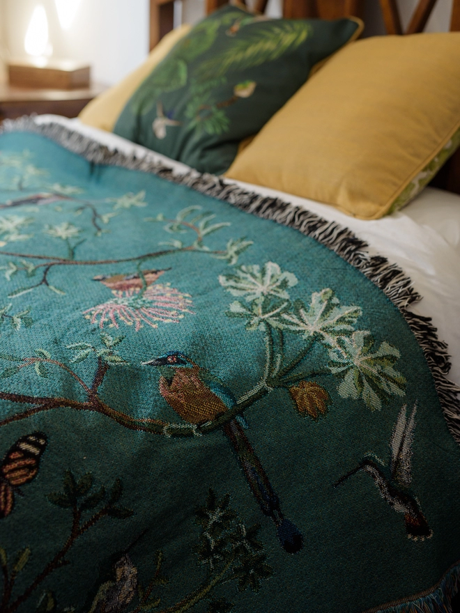 Forest Flight Blanket by Arcana seen on a bed with yellow and green pillows.