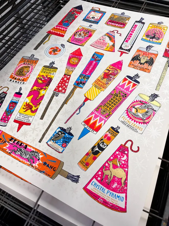 Fireworks Screenprint Snap, Crackle, Pop, a collection of colourful fireworks on a white screenprint. It sits against a studio rack. 