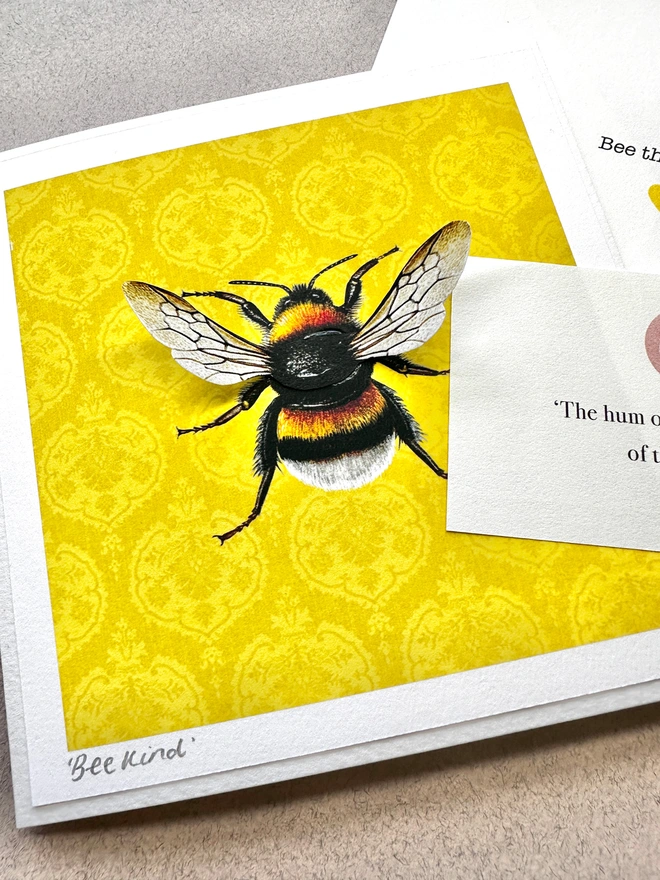 Close up of hand made card featuring a white tailed bumblebee with 3D paper wings on a golden yellow background.