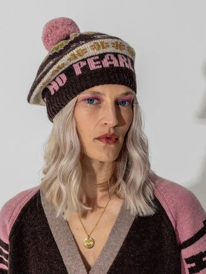 Model wearing the fairisle feminist beret in calamine and cocoa featuring the wording No Grit No Pearl