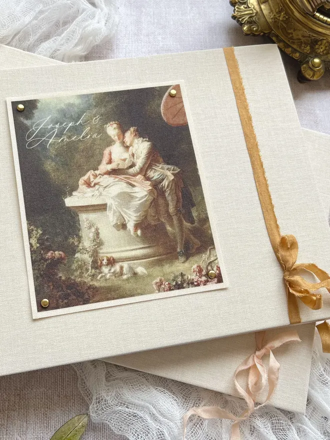 Luxury fabric printed wedding guest book featuring an images of lovers from an 18th century rococo work of art. Linen covered book finished with ribbon