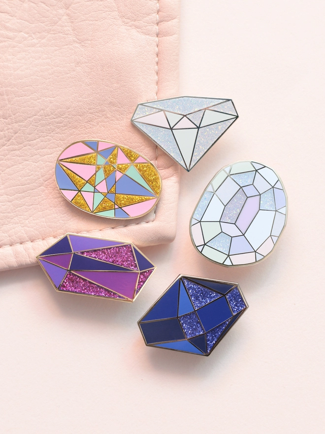 group of sparkly birthstone enamel pins laying on a pink jacket