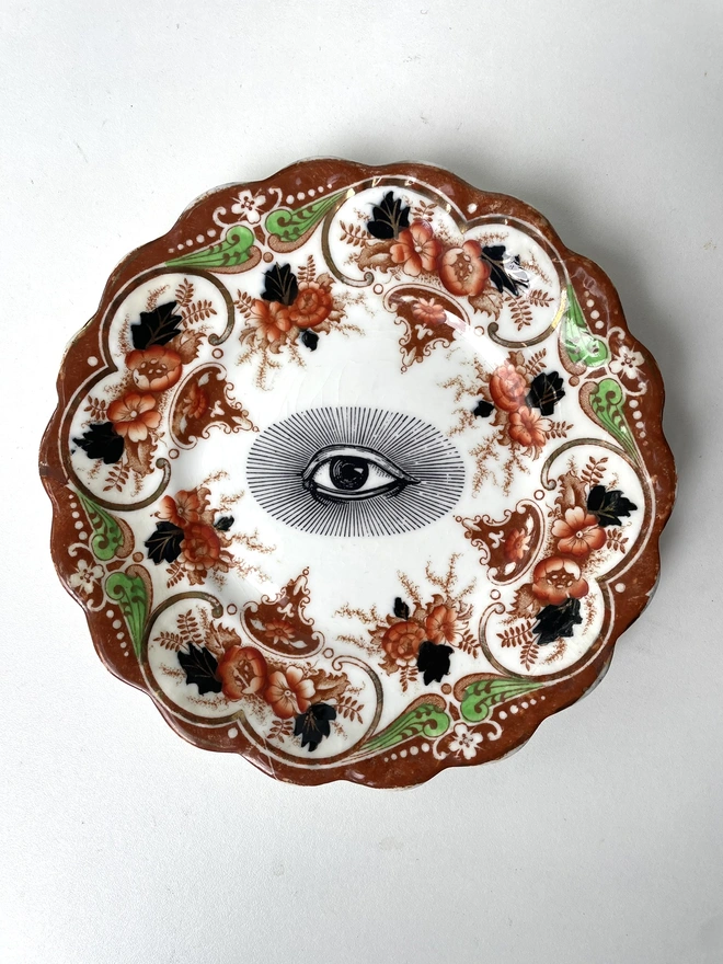 an ornate vintage plate with detailed border and in the centre an vintage illustration of an eye