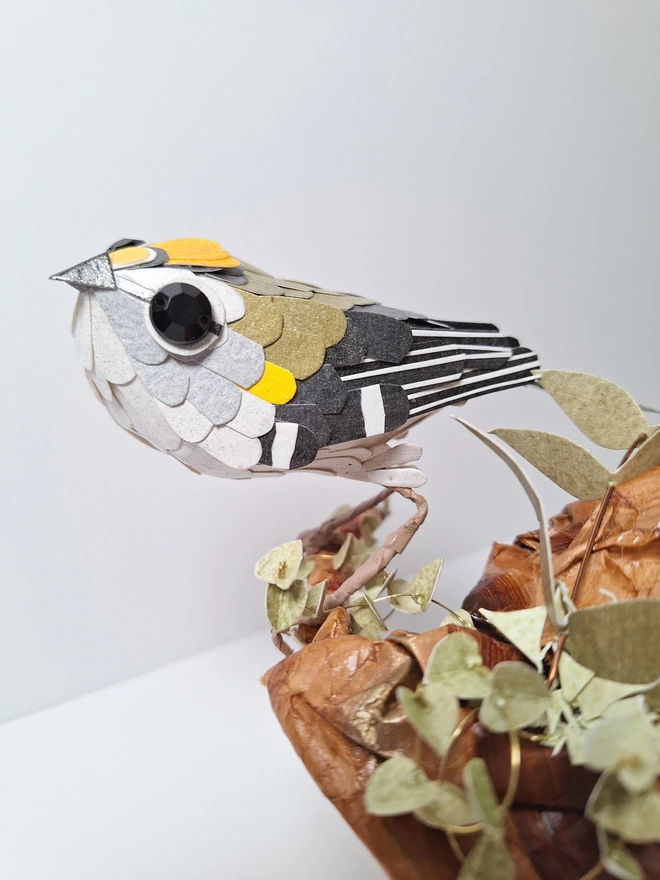 Firecrest paper bird sculpture, perched on a tree stump. This is a close up side view of the handmade garden bird, with its distinctive markings.