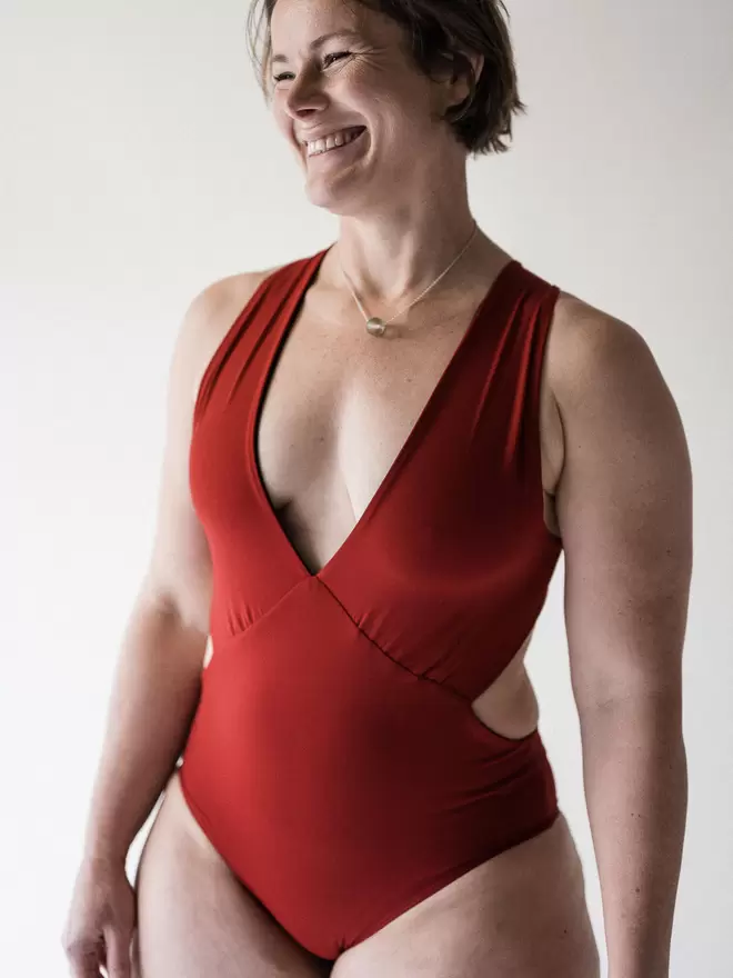 Laughing woman in studio with short brown hair, wearing red Davy J Sustainable Waterwear cutout swimsuit with plunging neckline