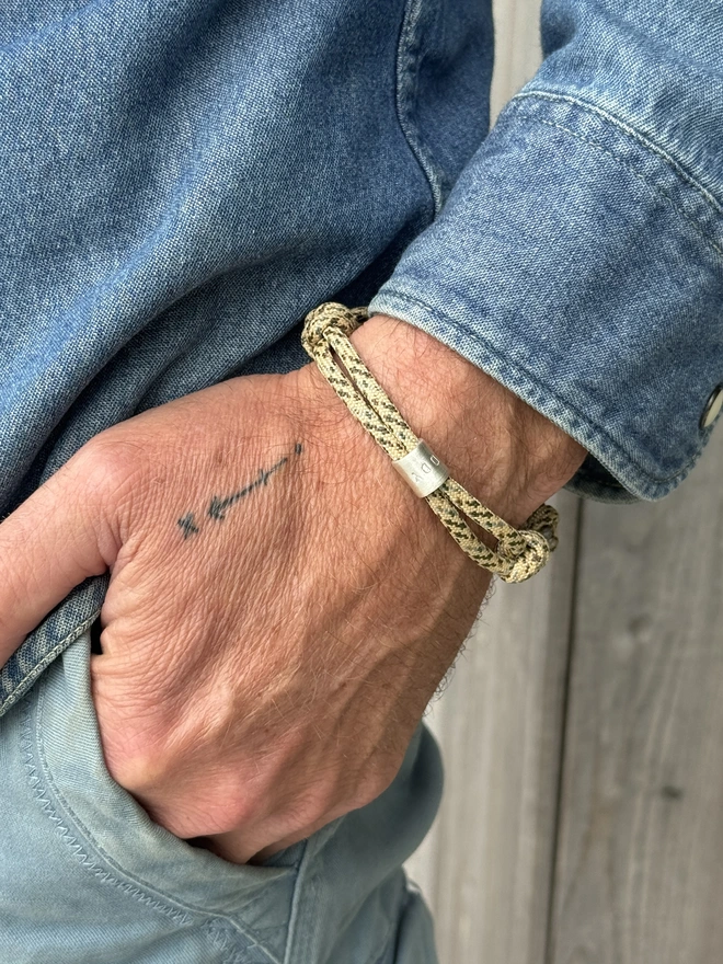 men's personalised drift paracord bracelet. a close up of a man's arm in a denim shirt wearing a sand coloured paracord bracelet.