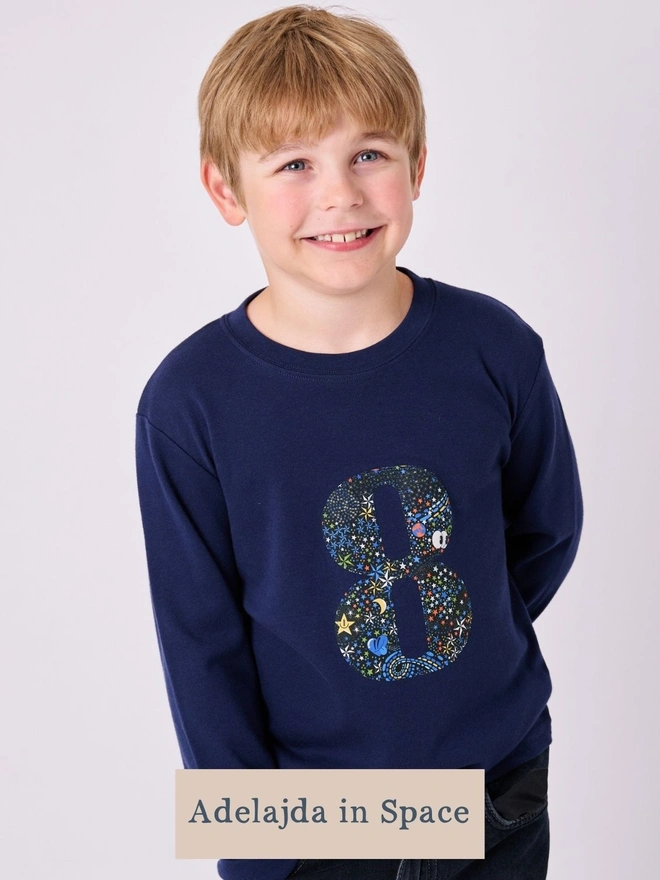  A 3 year old boy wearing a navy birthday t-shirt with a number 3 cut from liberty star and planet print on the front