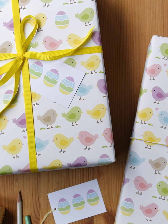 A gift wrapped in pastel spring chicks wrapping paper tied with yellow ribbon is on a wooden floor.