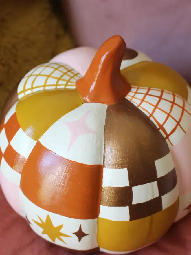 hand-painted celestial patchwork ceramic pumpkin. a ceramic pumpkin painted with patchwork colours of gold, pink, brown and stars and moons.