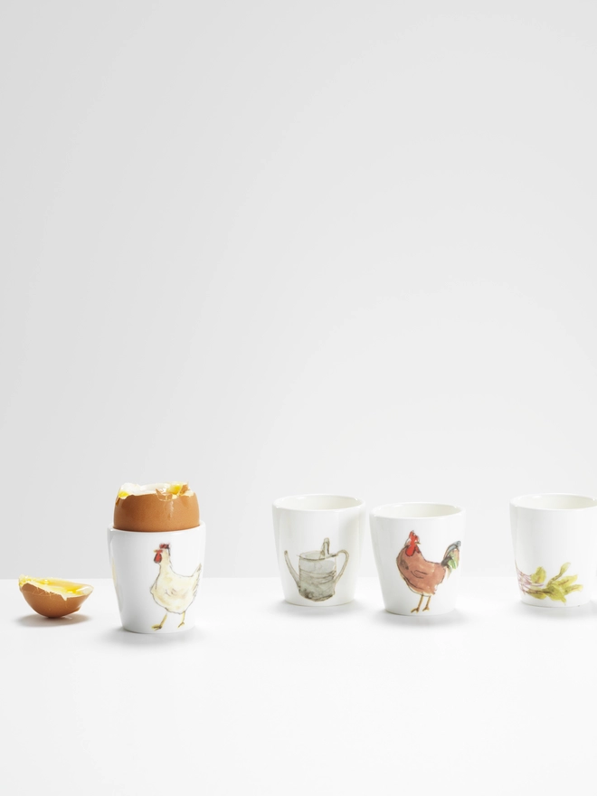 Photo of egg cups with egg in, illustrated with brown cockeral, white speckled hen, beetroots and watering can 