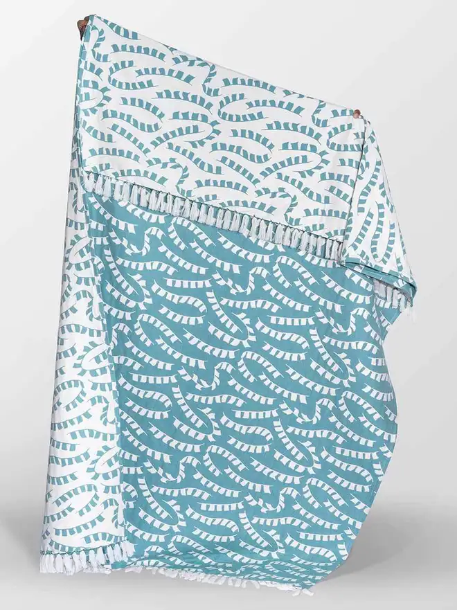 Teal Prayer Flag Woven Throw, a blue  throw held by a person against a white backdrop. 