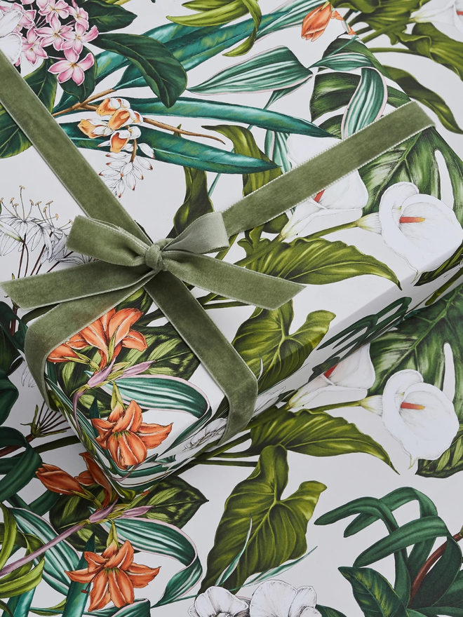 palm house tropics floral gift wrap sheet. a box wrapped in white illustrated leafy gift wrap with a purple ribbon.