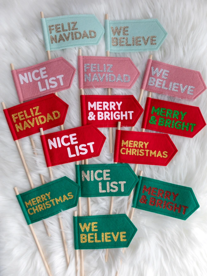 A range of christmas flags in a variety of colours and messages. The flags are made from felt and the text is written in bold glitter letters