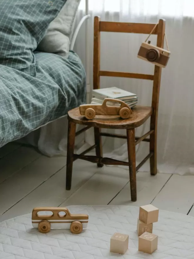 2 wooden toy cars in shot one on a wooden car and the other on a white rug