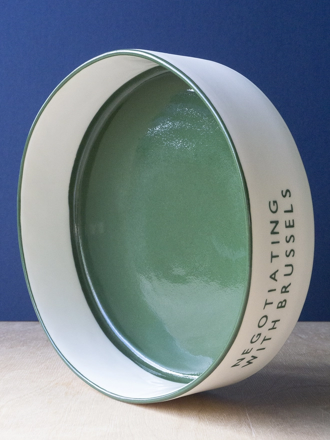 Ceramic porcelain dish with Negotiating with Brussels written on the side. A white Christmas serving dish with green rim and interior.