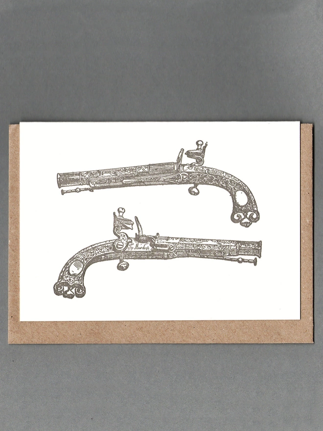 White card with grey illustration of two pistols with brown card behind