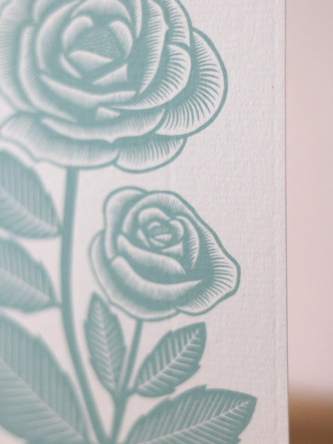 A greetings card feature a teal rose design based on an original linocut print