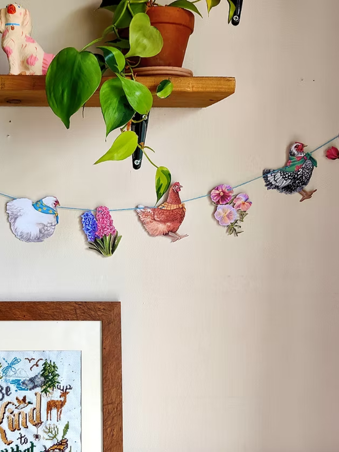 illustrated easter chickens and spring flowers garland. chickens wearing easter bonnets on bunting, hung on a wall.