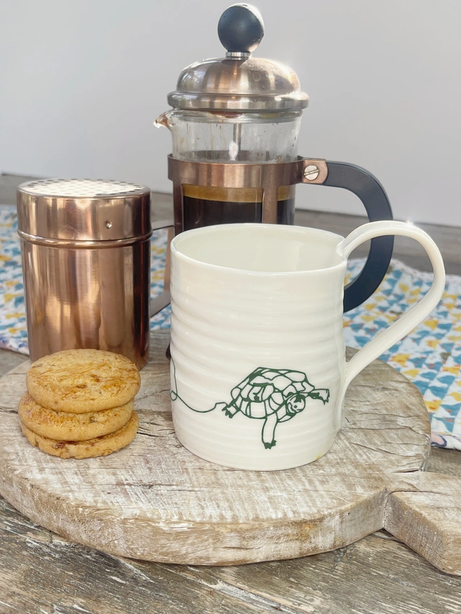 Hand thrown porcelain mug with tortoise design in a coffee scene with coffee pot and biscuit stack