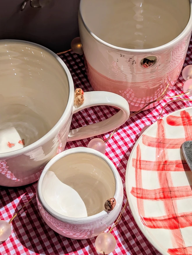 robin cup jug and tealight on a gingham tablecloth each pottery piece has a robin or two birds attached 