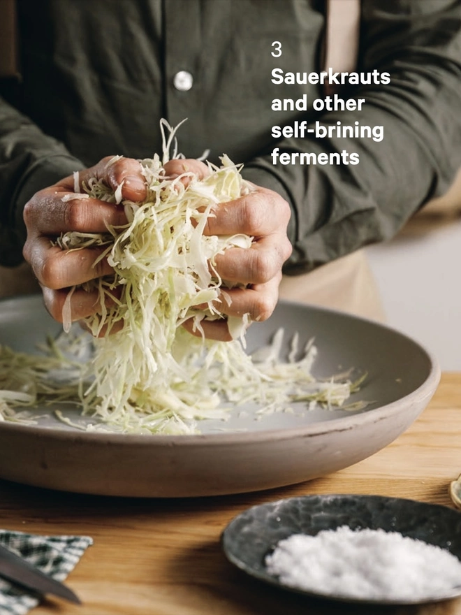 A man's hands scrunching sliced cabbage over a bowl to make sauerkraut