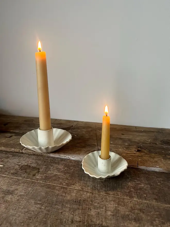 Handmade White Ceramic Candlestick Holder, a pair of white candle holders on a wooden surface. They are accompanied by lit candles. 
