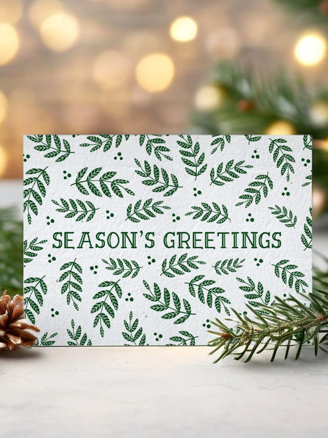 Christmas card with 'Seasons Greetings' on it surrounded by green leaves. The card is in a Christmas scene