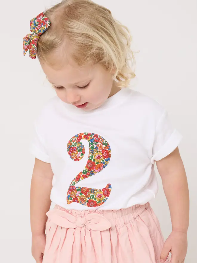 a 2 year old girl wearing a white birthday t-shirt with a number 2 cut from liberty floral print on the front
