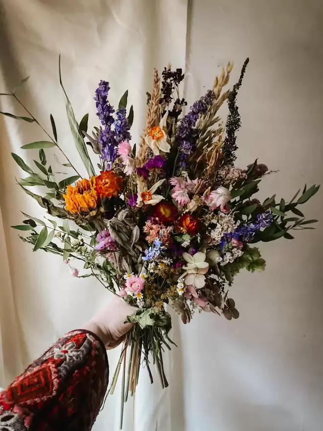 Purple and Orange Dried Flower bouquet held by a hand.