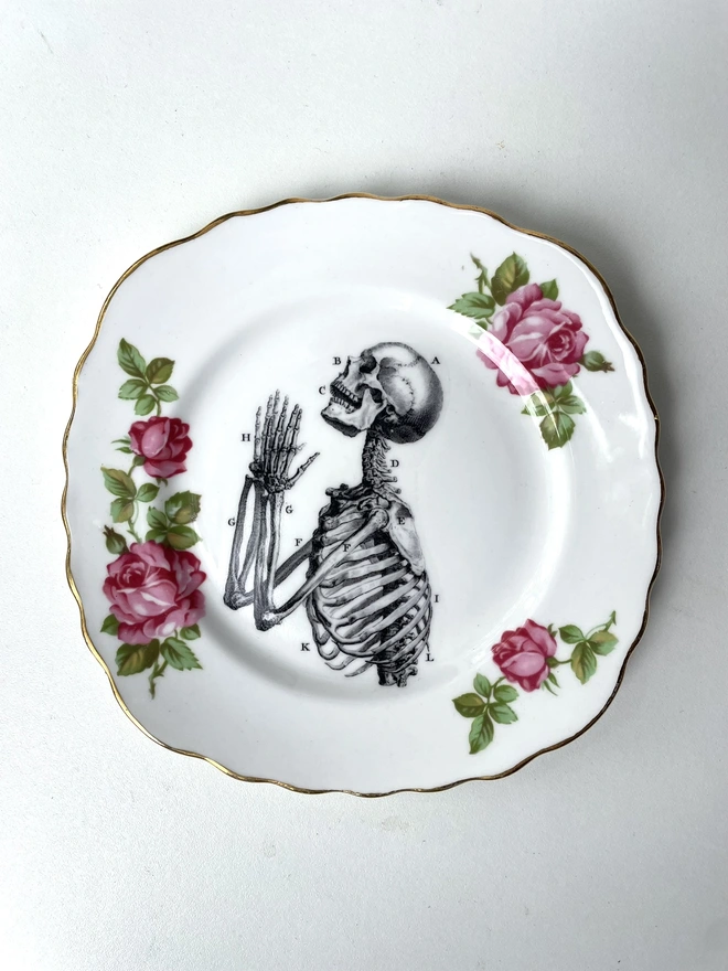 vintage plate with an ornate border, with a printed vintage illustration of a praying skeleton in the middle