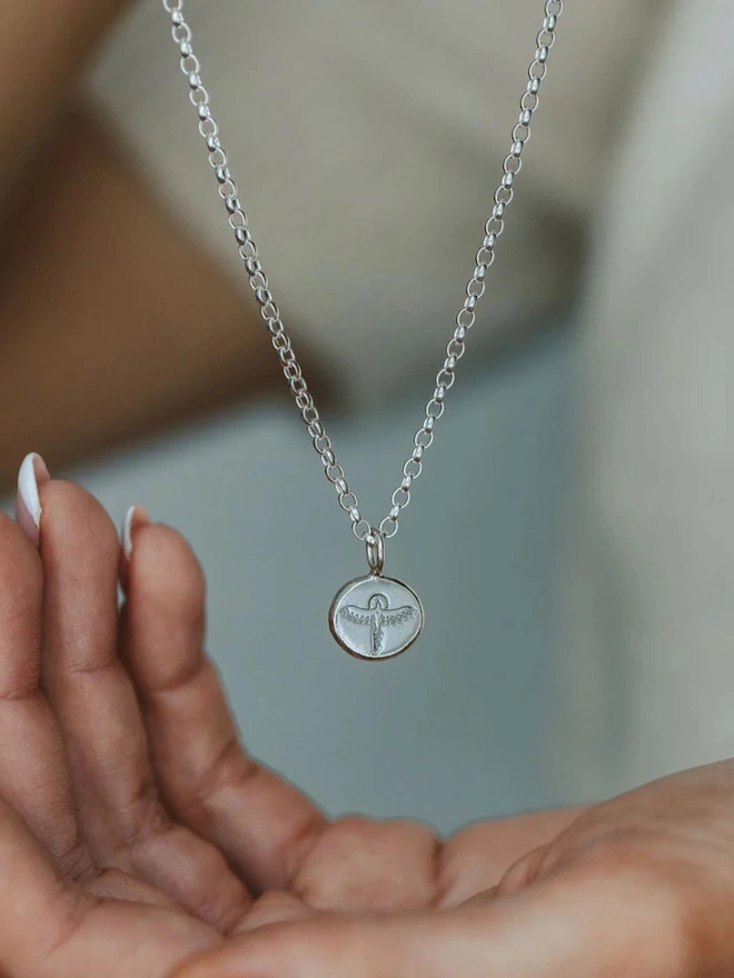 a hanging Sterling silver Phoenix Pebble Necklace above a hand