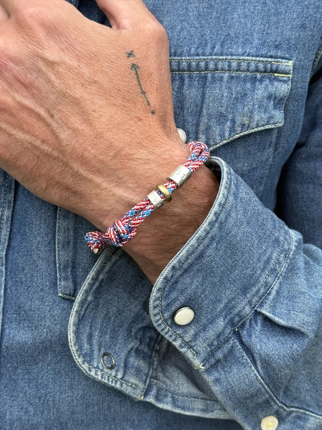 men's personalised drift paracord bracelet. a close up of a man's arm in a denim shirt wearing a red and blue paracord bracelet.