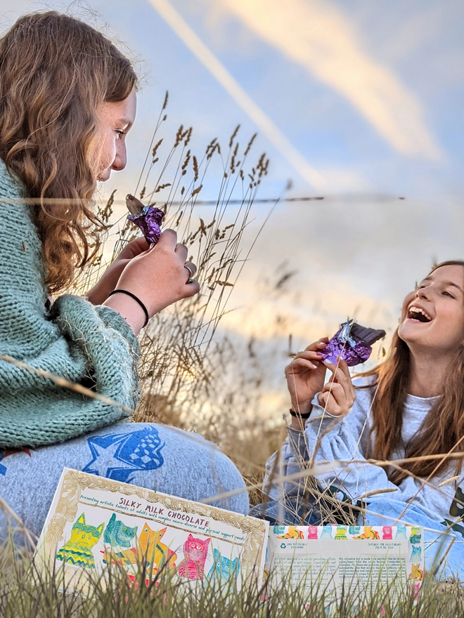 Girls in a field enjoying silky smooth chocolate bar with hand drawn colourful cat wrapper 