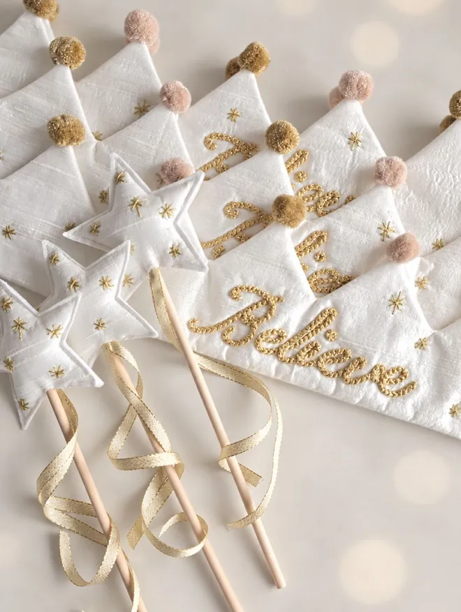 Handmade white silk Believe Christmas crowns with matching star wands, metallic gold embroidery, gold star details and soft blush and antique gold pom-poms.
